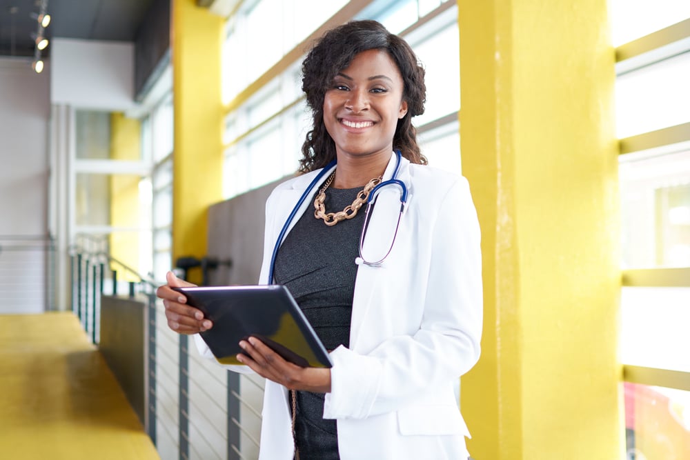 Female doctor holding her patient chart on digital tablet in bright modern hospital