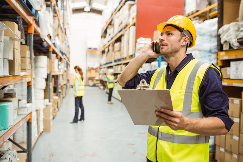 Warehouse worker talking on the phone holding clipboard in a large warehouse