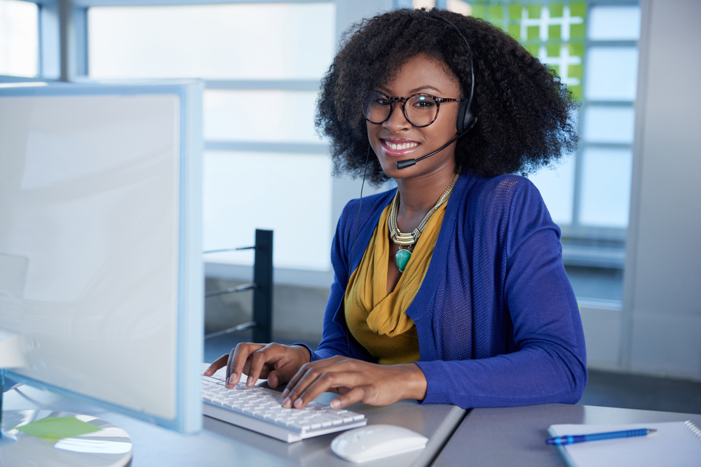 Portrait of a smiling customer service representative with an afro at the computer using headset